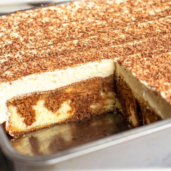 A large tiramisu cake with a slice removed, showing layers of cream and coffee-soaked cake.