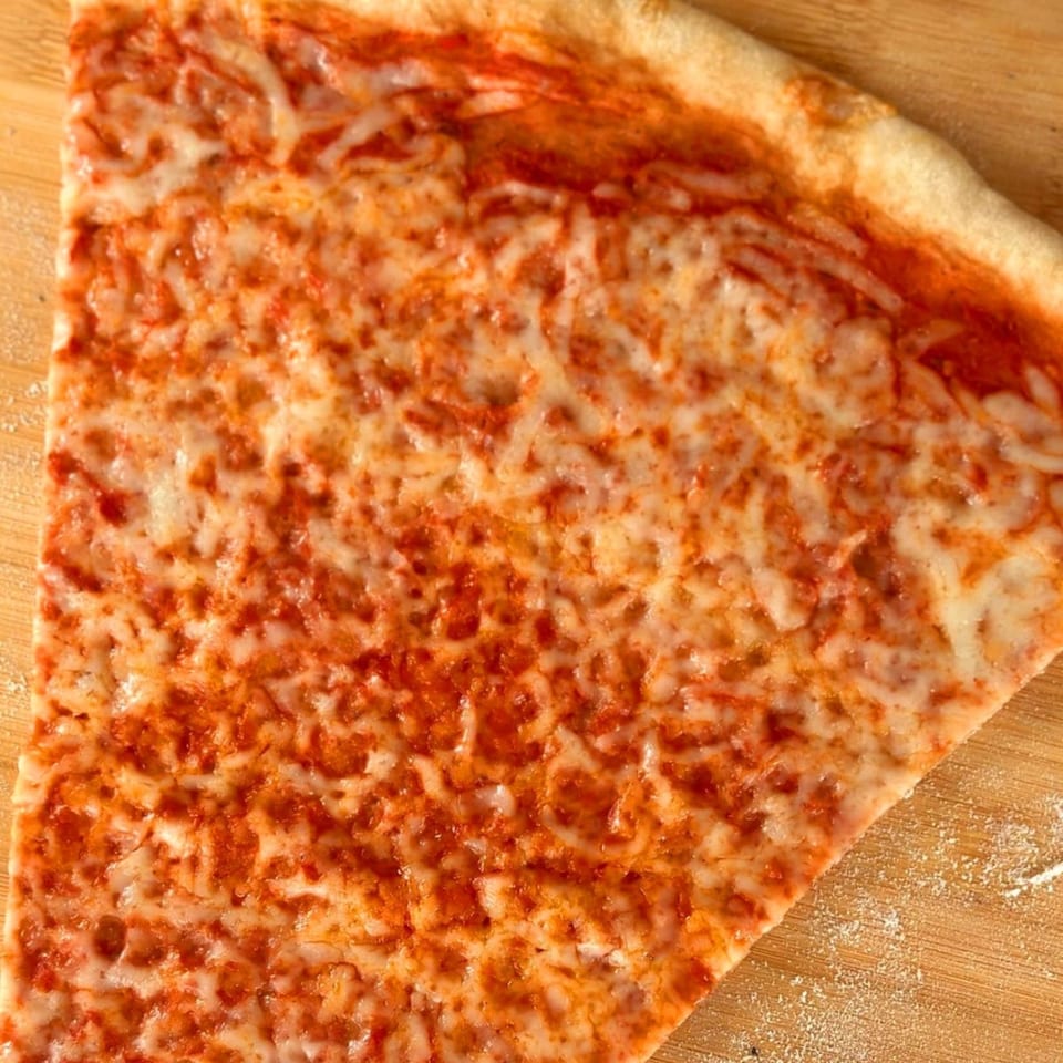 A close-up of a single slice of Why Not Pizza's classic cheese pizza on a wooden surface.