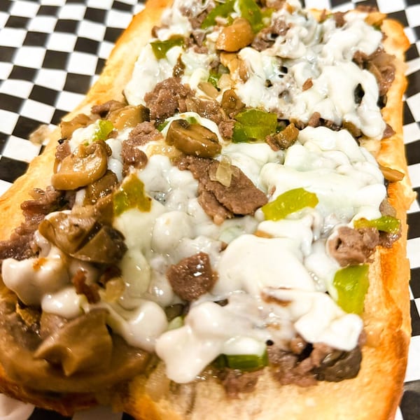 Cheesesteak sub with melted cheese, steak, green peppers, and mushrooms on a checkered paper.