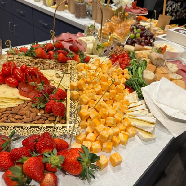 A large charcuterie board features cheeses, meats, strawberries, tomatoes, nuts, and bread.
