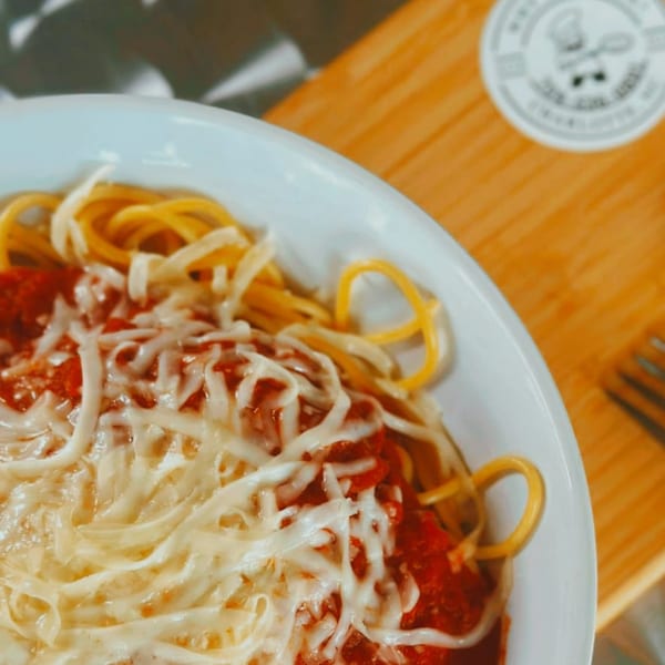 A white bowl filled with spaghetti, red sauce, and melted shredded cheese, on a wooden surface.