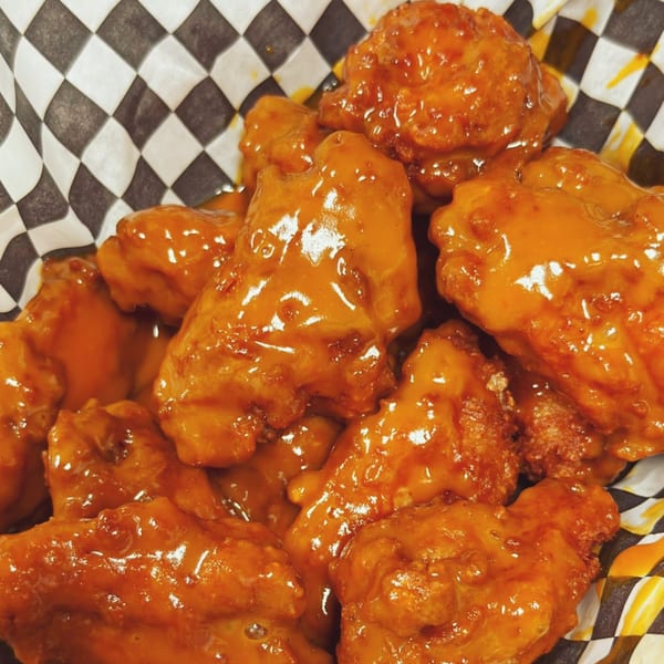 Close-up of golden-orange boneless chicken wings in a black and white checkered paper basket.