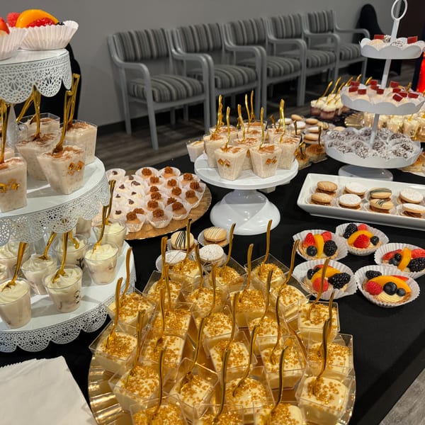 A dessert table laden with various small pastries, fruit tarts, and creamy desserts in cups.