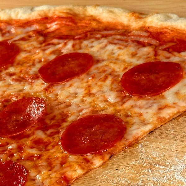 Close-up of a pepperoni pizza slice from Why Not Pizza, with melted cheese and a crispy crust.